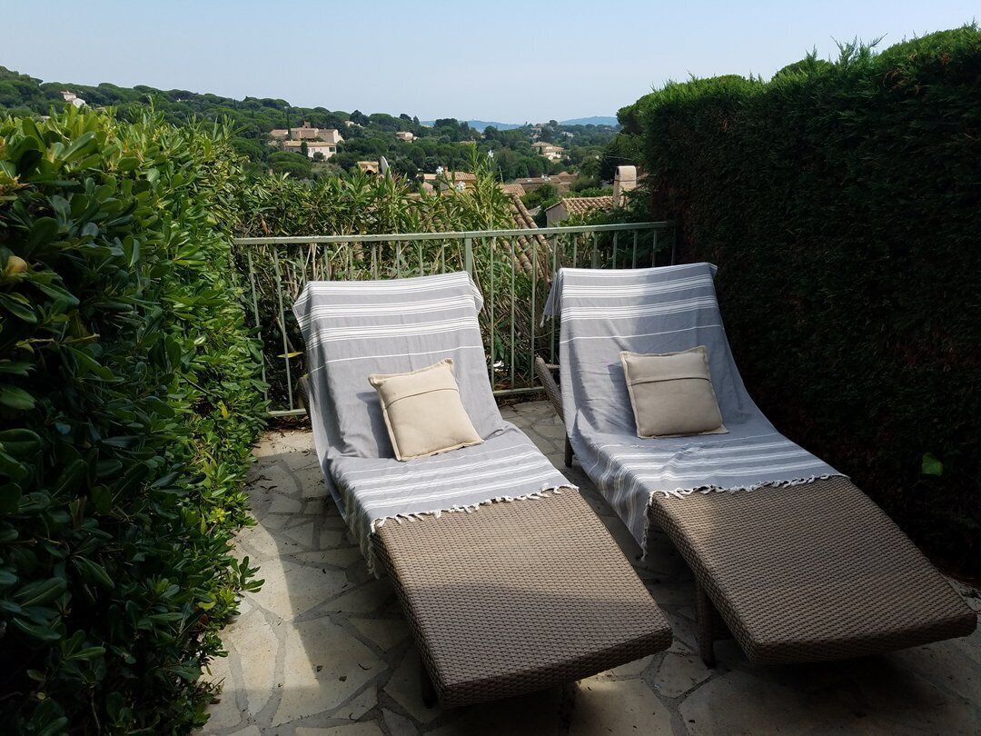Two lounge chairs with striped cushions, a stone patio, and a view of a village in the background.