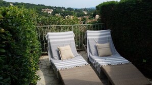 Two lounge chairs with striped cushions, a stone patio, and a view of a village in the background. - Renovated mas with beautiful sea views, accommodating up to 4 guests. (SAINTE MAXIME)