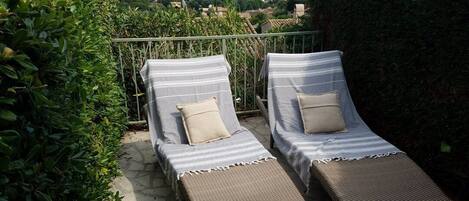 Two lounge chairs with striped cushions, a stone patio, and a view of a village in the background.