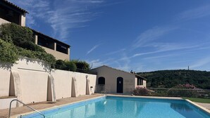 A swimming pool with a clear blue water, a white wall, and a building with a dark door in the background. - Renovated mas with beautiful sea views, accommodating up to 4 guests. (SAINTE MAXIME)