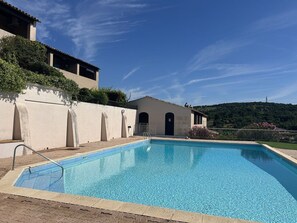 Ein Swimmingpool mit klarem, blauem Wasser, einer weißen Wand und einem Gebäude mit einer dunklen Tür im Hintergrund.