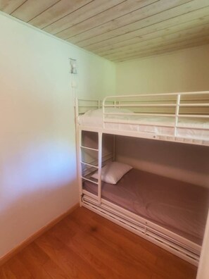 Ein Schlafraum mit Etagenbetten, Holzboden und weißer Wand.