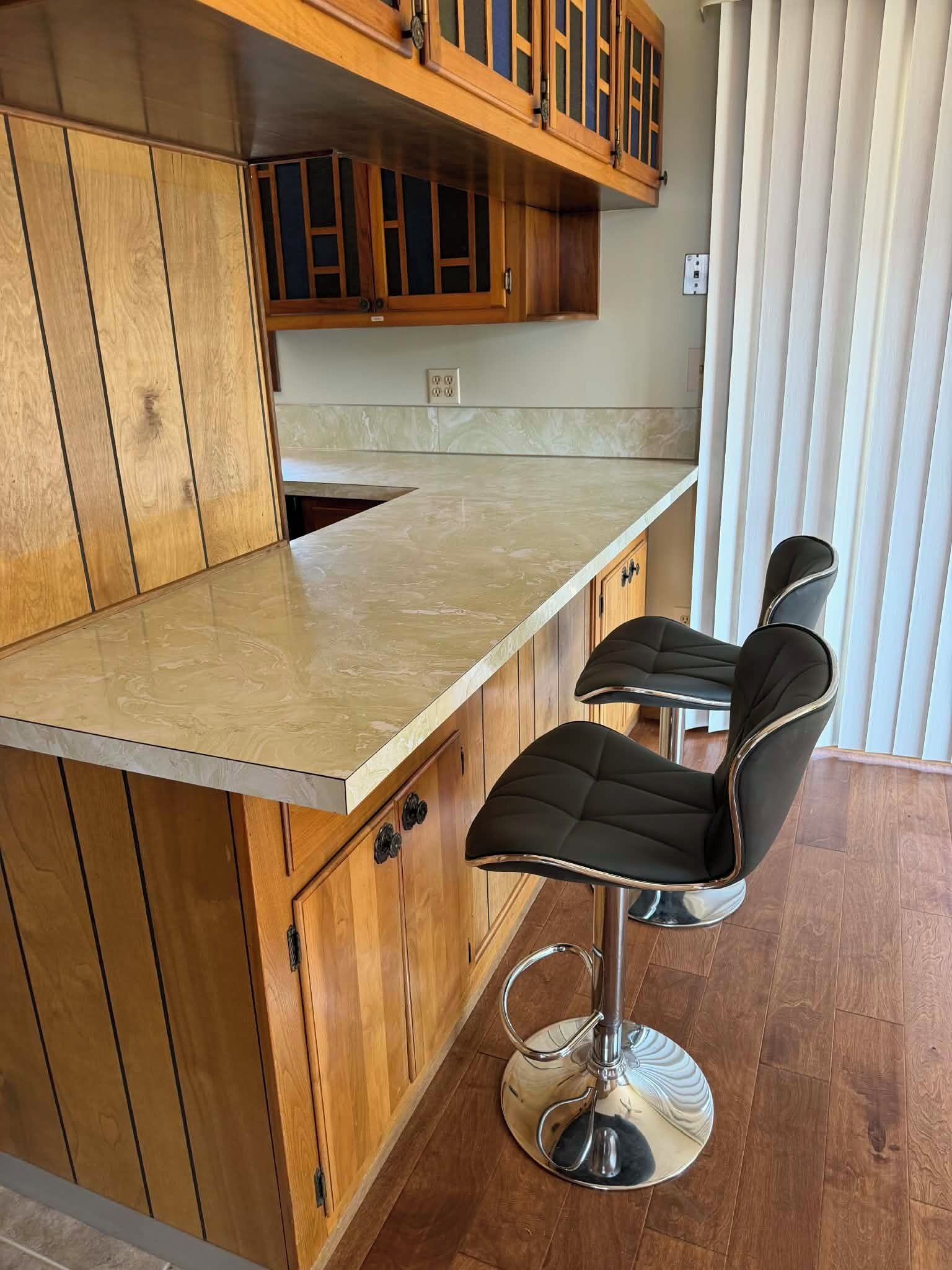 A kitchen with wooden cabinets, a marble countertop, and two black bar stools.