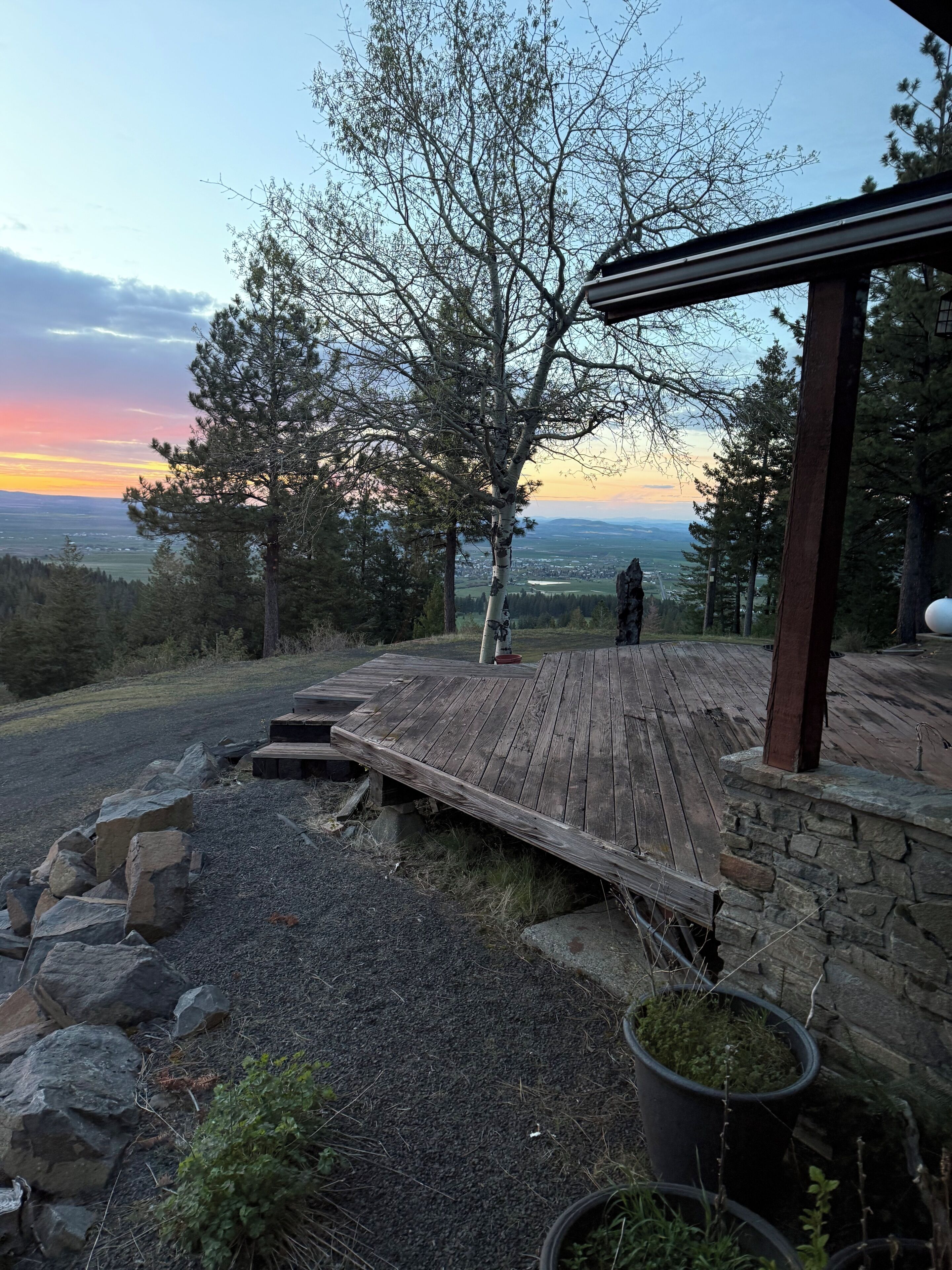 Une terrasse en bois avec un mur en pierre, une vue sur le paysage et un arbre.