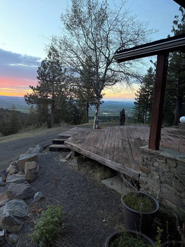 A wooden deck with a stone wall, a view of the landscape, and a tree.