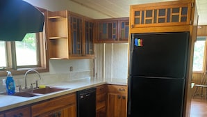 Una cocina con armarios de madera, un refrigerador negro, un lavavajillas y una ventana con vista a la vegetación.
