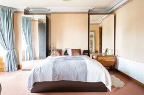 A bedroom with a large bed, a dresser, a mirror, and a window with curtains. - Victorian Rooms (Belfast)