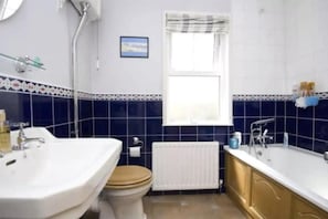 Un baño con lavamanos, inodoro y bañera blancos, una ventana con vistas y un radiador.
