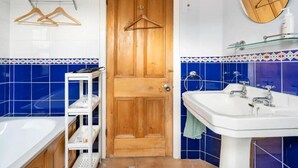 Un baño con puerta de madera, un lavabo blanco, un espejo y un estante con artículos de aseo.