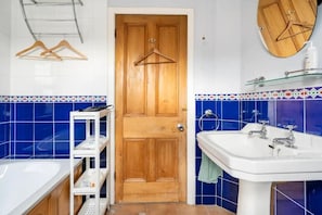 Un baño con puerta de madera, un lavabo blanco, un espejo y un estante con artículos de aseo.