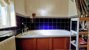 Un baño con bañera, una ventana y un estante con artículos de aseo.