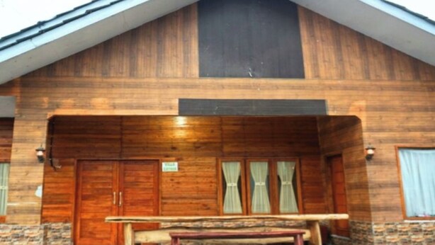 Una construcción de madera con techo inclinado, una puerta de madera grande y un banco al frente.