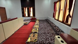 Una habitación con alfombra roja, cojines estampados, un banco y un ventanal con cortinas.