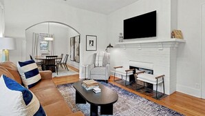 En moderne stue med pejs, sofa, sofabord og et tv hængt over pejsen.
