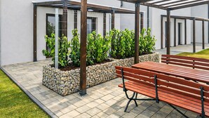 A patio area with a wooden bench, stone planters with green plants, and a metal pergola structure. - 2 bedroom beautiful home in Mrzezyno (Mrzezyno)