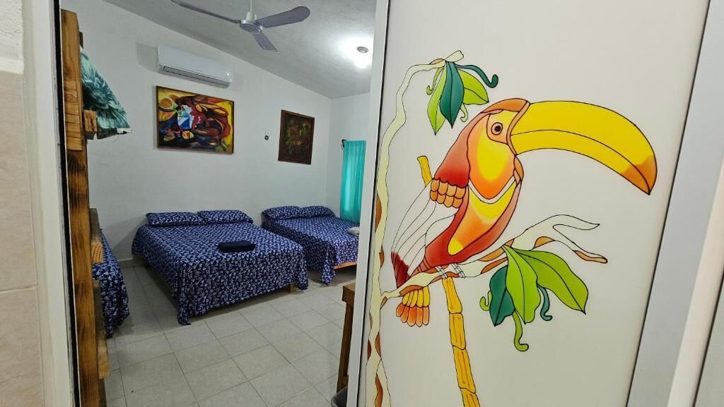 Una habitación con dos camas, un ventilador de techo y un cuadro en la pared con un tucán.