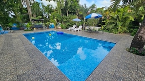 Uma piscina retangular com água azul cristalina, rodeada por um deck revestido com azulejos.