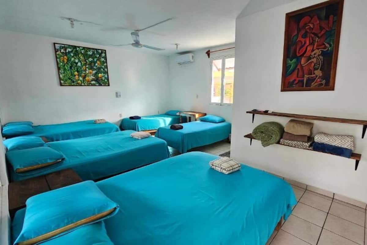 Een kamer met vier bedden, een plafondventilator en kunstwerken aan de muur.