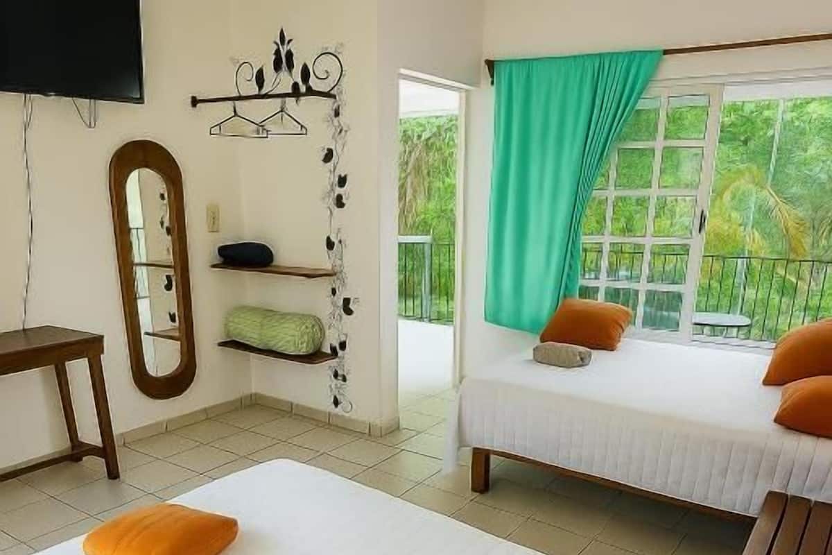 Een hotelkamer met een groot bed, een kleiner bed, een televisie, een spiegel en een balkon met uitzicht.