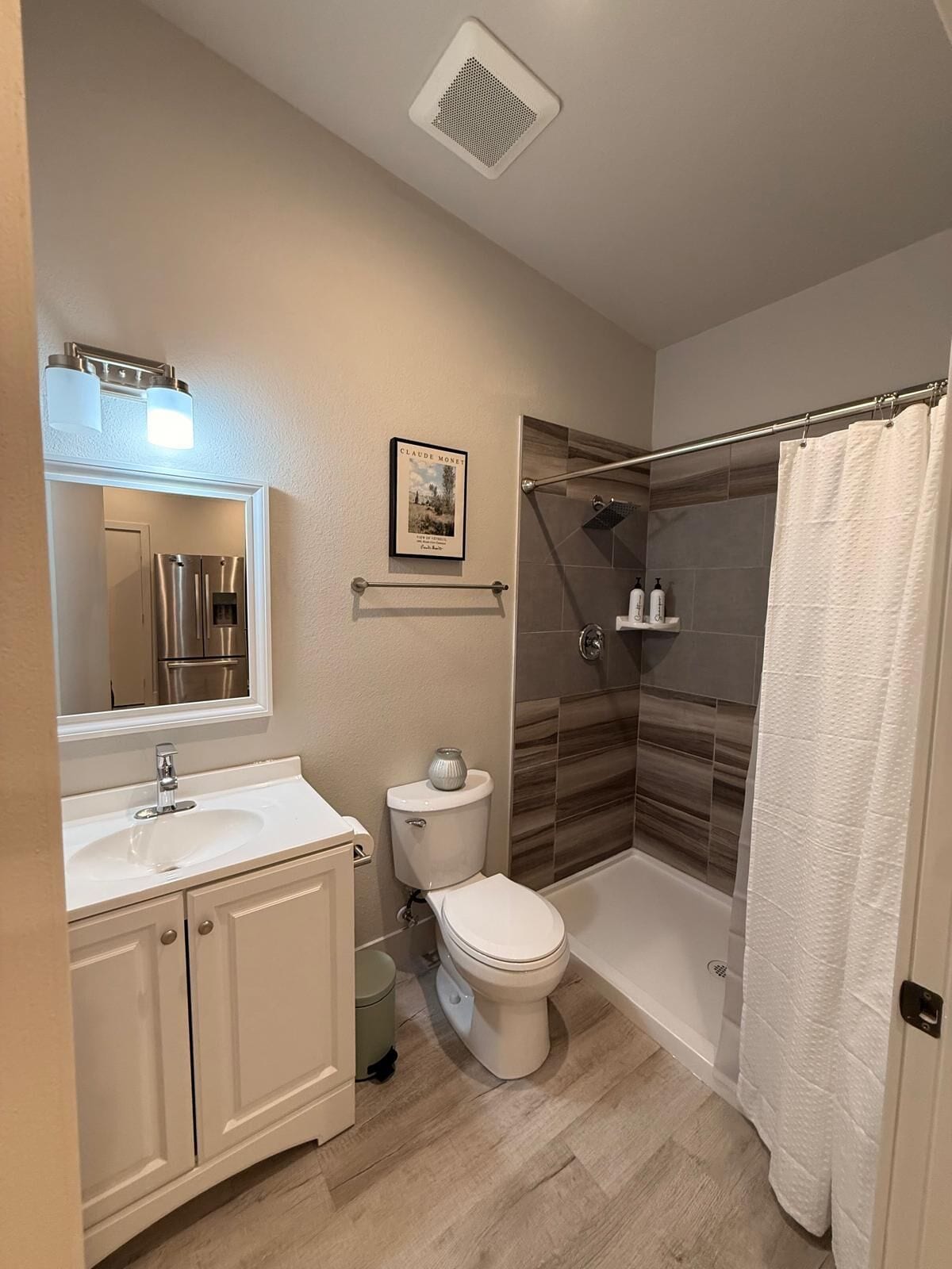 Un baño moderno con ducha, inodoro, lavamanos y un cuadro en la pared.