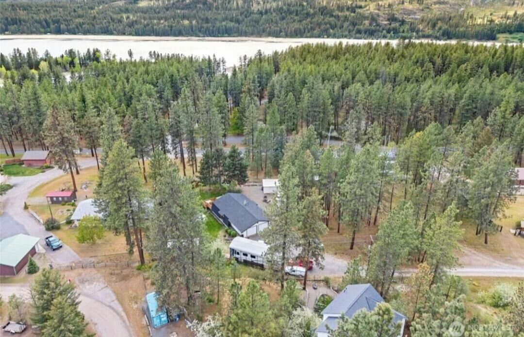 Et boligområde med huse omgivet af tæt skov, en sø i baggrunden og en klar himmel.