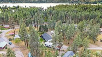 Et boligområde med huse omgivet af tæt skov, en sø i baggrunden og en klar himmel.
