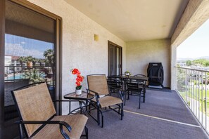 A balcony with a table and chairs, a grill, and a view of a pool and palm trees.