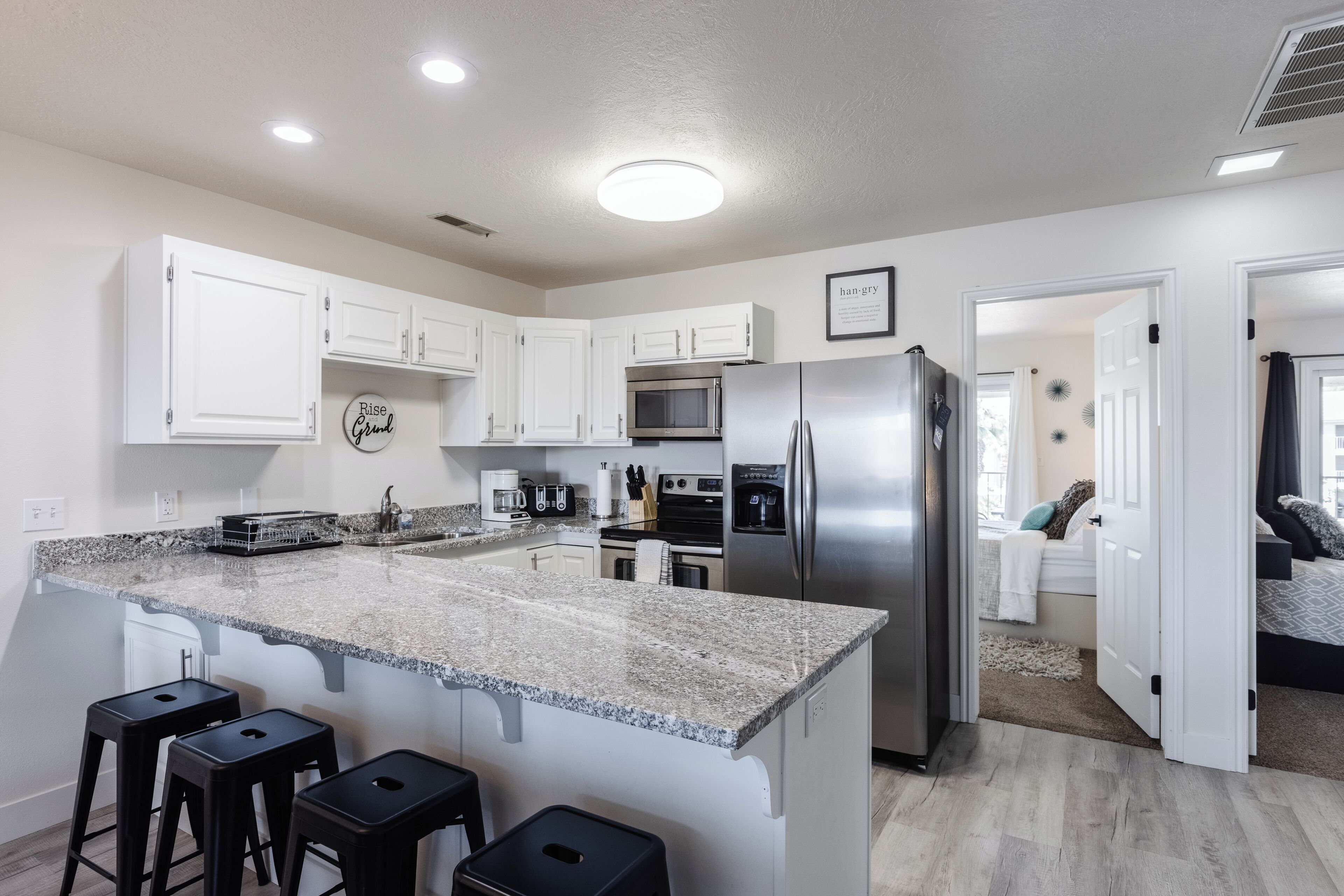 A modern kitchen with white cabinets, a granite countertop, stainless steel appliances, and a bar stool area.