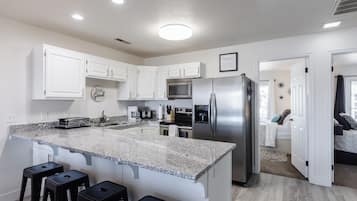 A modern kitchen with white cabinets, a granite countertop, stainless steel appliances, and a bar stool area.