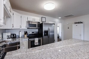 A modern kitchen with white cabinets, stainless steel appliances, granite countertops, and a 'family' sign on the wall.