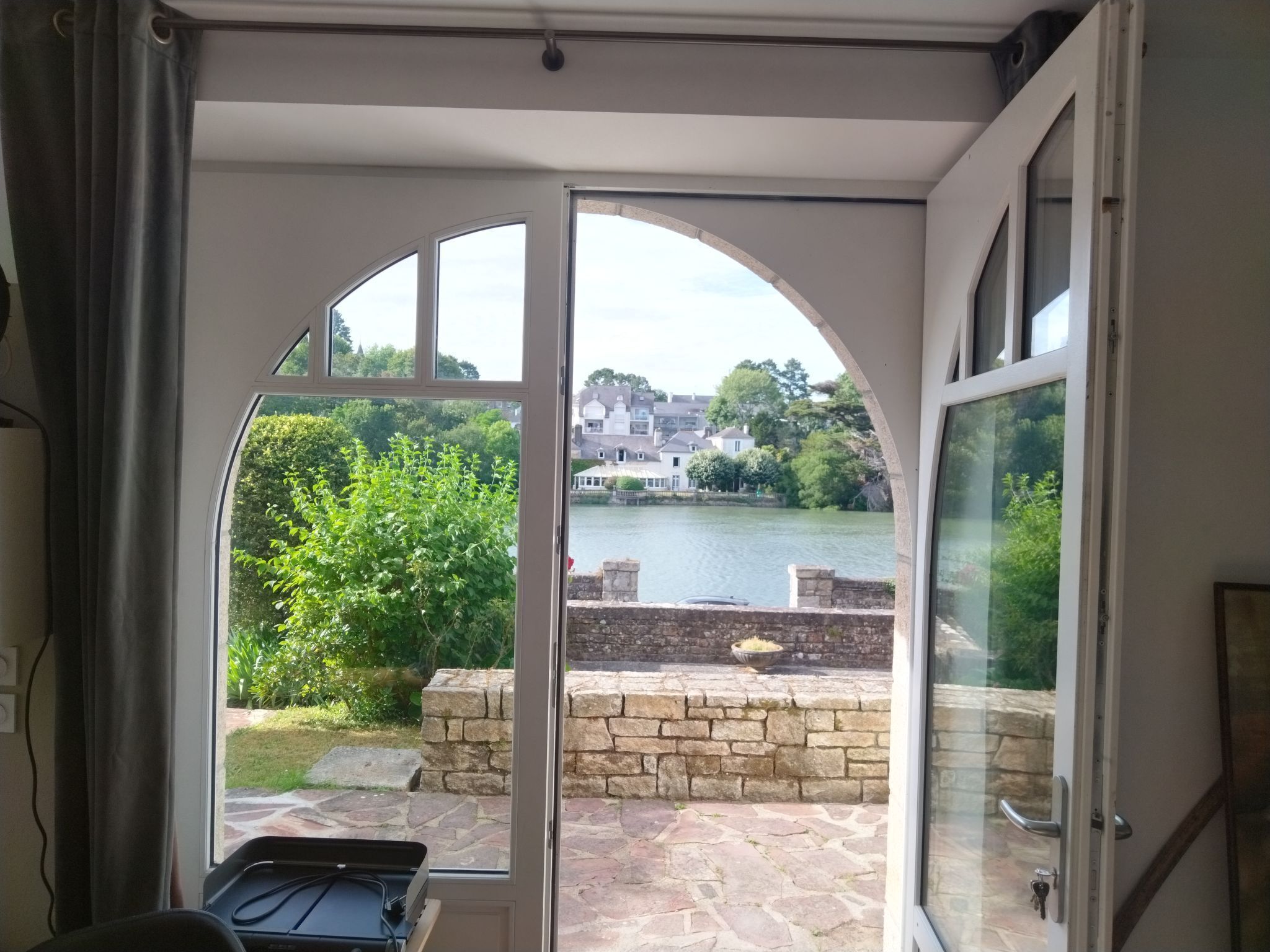 Ein Zimmer mit Seeblick, einer Steinterrasse und viel Grün.
