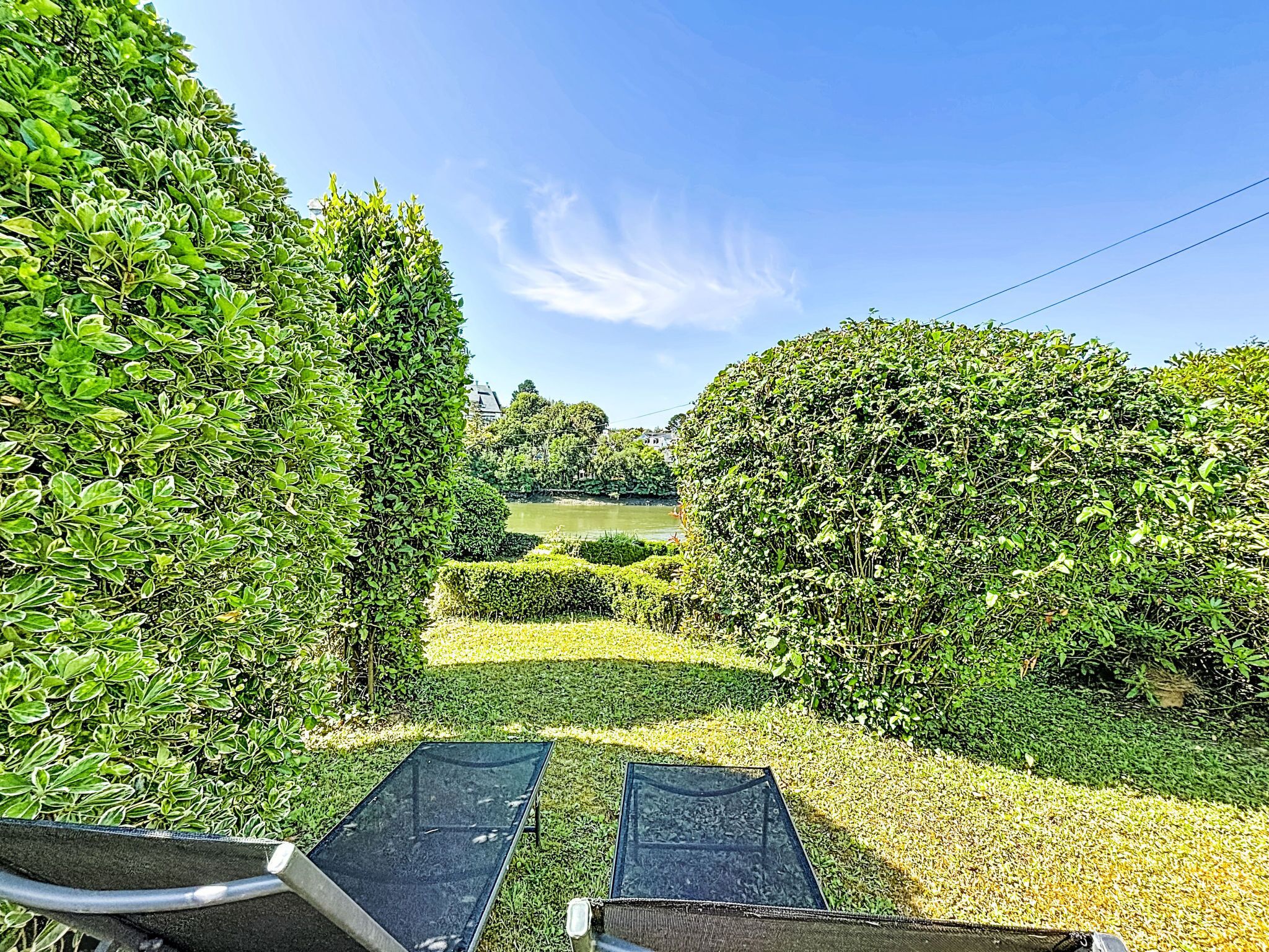 Un jardin avec des haies soigneusement taillées et une vue dégagée sur un lac.