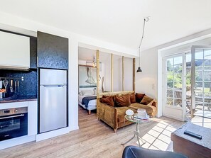 A compact living space with a kitchenette, a sofa, a dining area, and a sliding glass door leading to an outdoor patio. - La rivière St Goustan by Interhome (Auray)