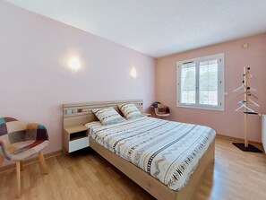 Une chambre à coucher avec un lit en bois, une chaise, une fenêtre et un porte-manteau fixé au mur.