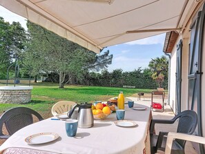 Ein Essbereich im Freien mit einem für das Frühstück gedecktem Tisch, einer Steinstruktur und Blick auf einen Garten.