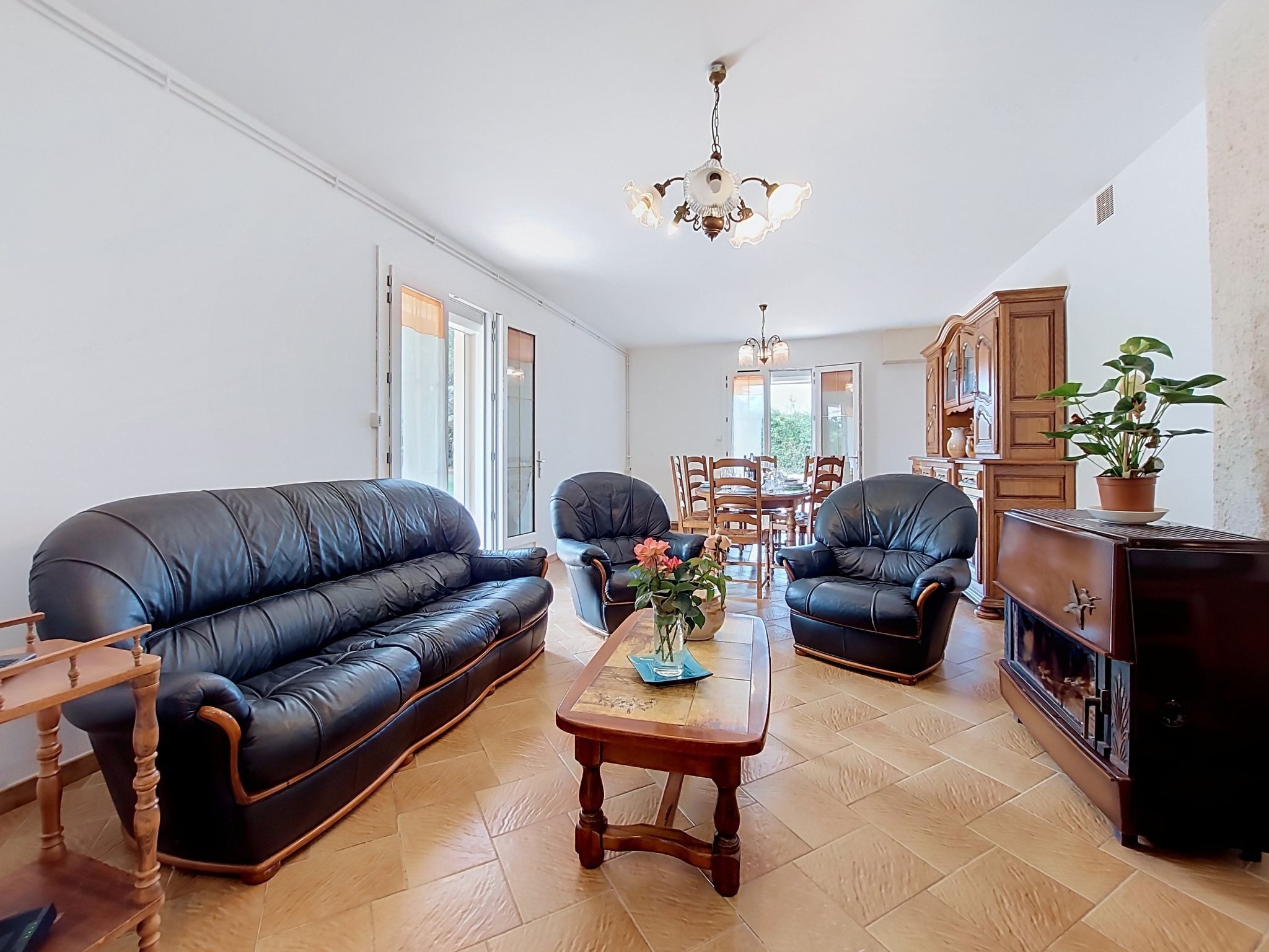 A living room with a black leather sofa, two armchairs, a wooden coffee table, and a dining area in the background.