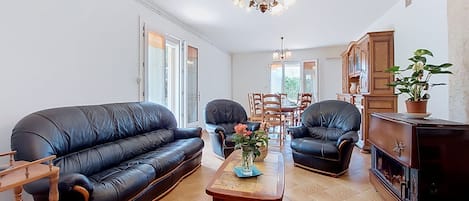 A living room with a black leather sofa, two armchairs, a wooden coffee table, and a dining area in the background.