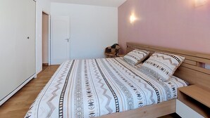 Un dormitorio con cama, mesitas de noche, una silla, una puerta y una lámpara fijada a la pared.