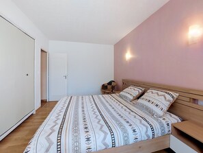 Ein Schlafzimmer mit Bett, Nachttischen, einem Sessel, einer Tür und einer Wandleuchte.