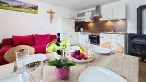 Uma sala de estar moderna com um sofá vermelho, uma mesa de jantar com um vaso cor-de-rosa e uma cozinha com armários brancos e uma lareira a lenha.