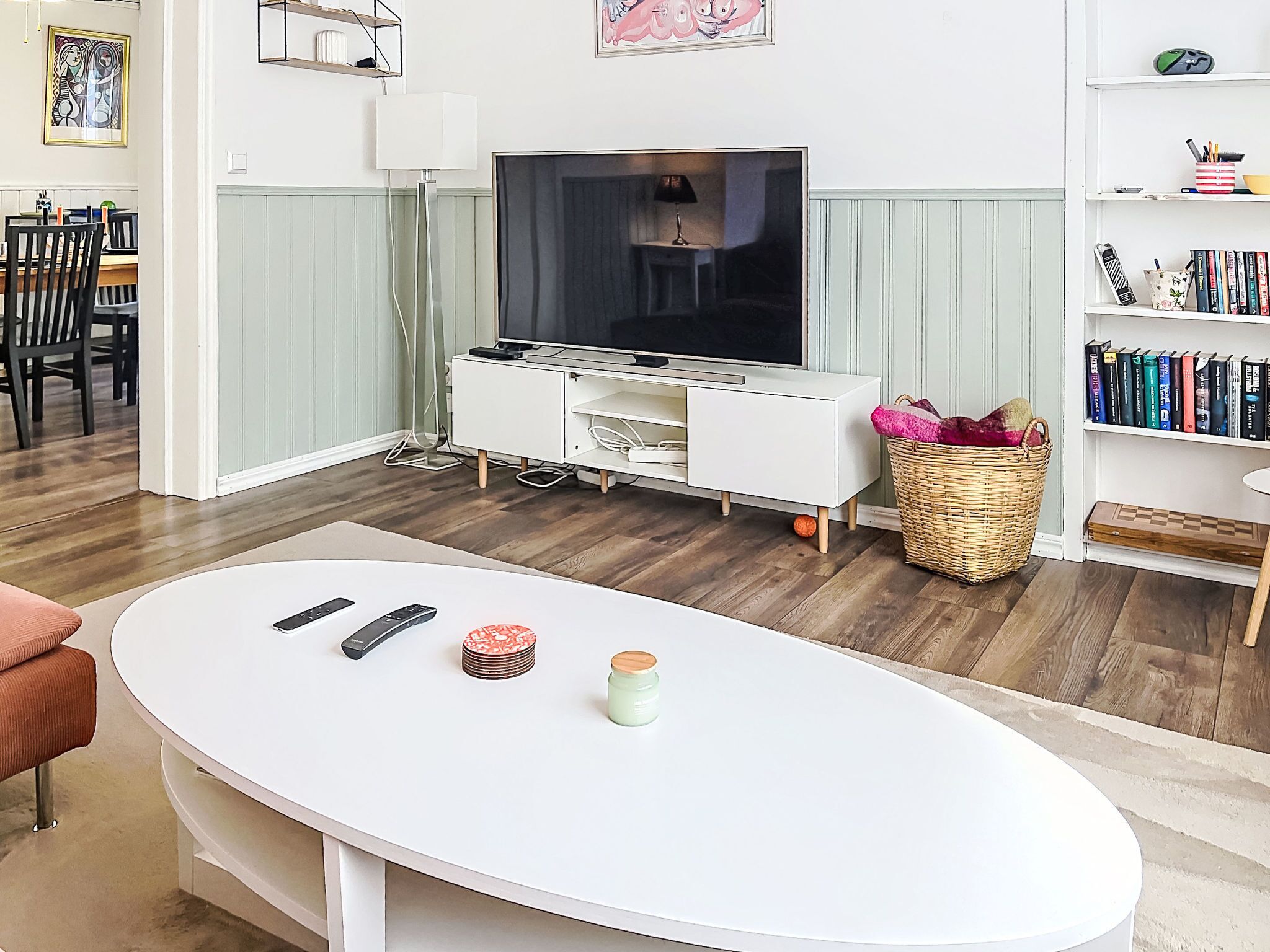 A living room with a TV, white entertainment unit, wooden flooring, a dining area, and a bookshelf.