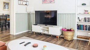 Ein Wohnzimmer mit Fernseher, weißem Unterhaltungsschrank, Holzboden, Essbereich und Bücherregal.