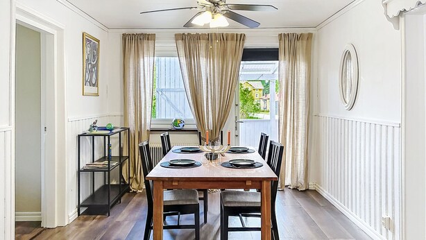 Ein Esszimmer mit einem Holztisch, gedeckt für vier Personen, einem Deckenventilator und einem Fenster mit Vorhängen.