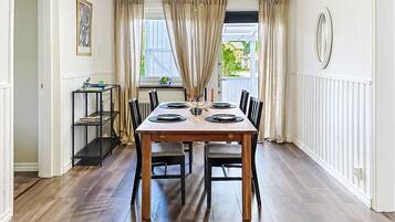 A dining room with a wooden table set for four, a ceiling fan, and a window with curtains.