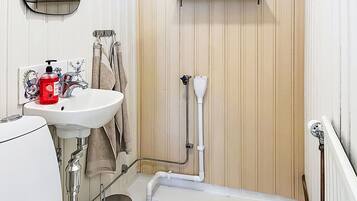 Et badeværelse med en hvid vask, et spejl, et håndklædetørrestativ, en bruser og en lille hylde med toiletartikler.
