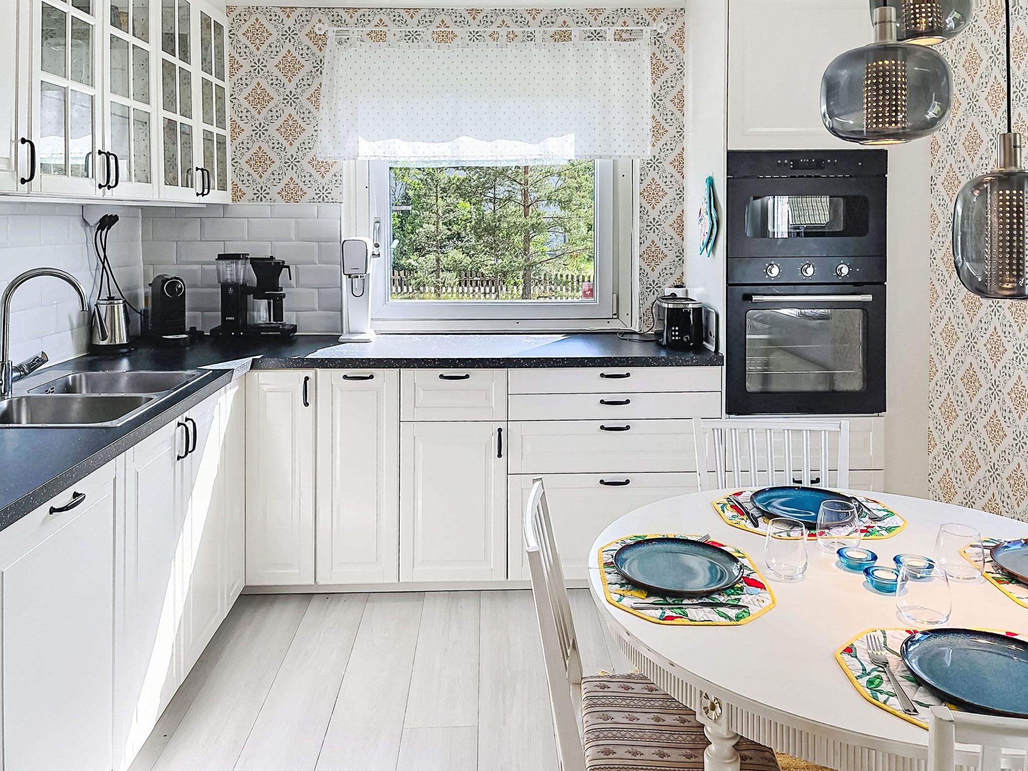 A kitchen with white cabinets, a black oven, a window with a view, and a dining table set for four.
