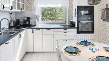 A kitchen with white cabinets, a black oven, a window with a view, and a dining table set for four.