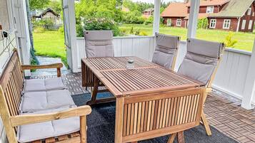 A wooden outdoor seating area with a table and chairs, a glass on the table, and a view of houses and greenery.