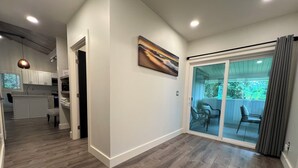 A modern kitchen with white cabinets, a dining area with a table and chairs, and a sliding glass door leading to a patio with outdoor furniture.