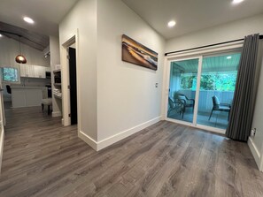 A modern kitchen with white cabinets, a dining area with a table and chairs, and a sliding glass door leading to a patio with outdoor furniture.